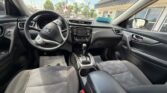 Interior of a car from the back seat: steering wheel, center console, gear shifter, and front seats, with a dealership lot outside.
