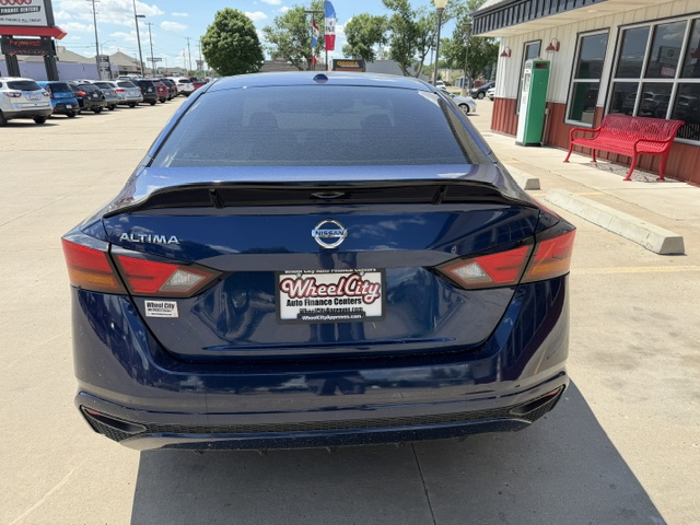 Rear view of a blue Nissan Altima parked in a dealership lot, with a Wheel City Auto Finance Centers license plate frame visible.