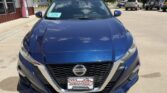 Front view of a metallic blue Nissan sedan parked in a dealership lot, Wheel City Auto Finance license plate frame visible on the front plate.