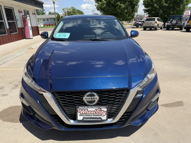 Front view of a metallic blue Nissan sedan parked in a dealership lot, Wheel City Auto Finance license plate frame visible on the front plate.