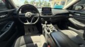 Interior of a Nissan sedan: steering wheel, center touchscreen, gear shifter, and black fabric seats.