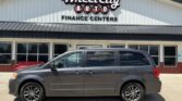 Gray minivan parked in front of Wheel City Auto Finance Centers dealership building with large sign above.