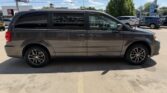 Side view of a gray minivan parked in a parking lot, with other cars and a dealership in the background.