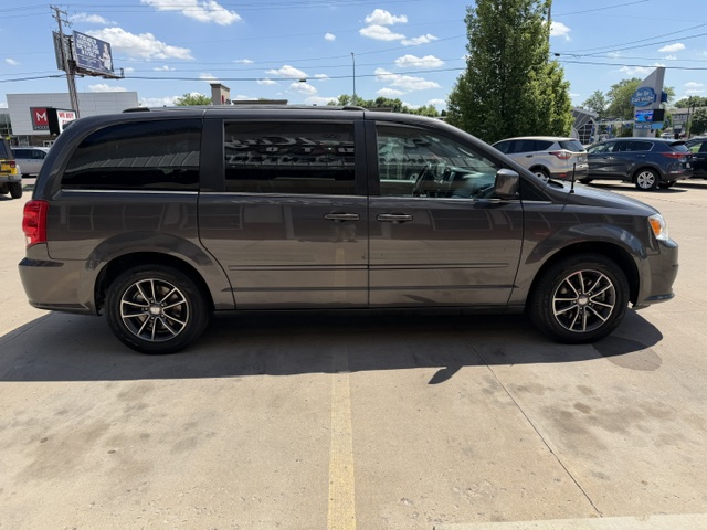 Side view of a gray minivan parked in a parking lot, with other cars and a dealership in the background.