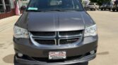 Front view of a gray Dodge minivan in a dealership lot, featuring a chrome grille and headlights, with a green sale sticker on the windshield.