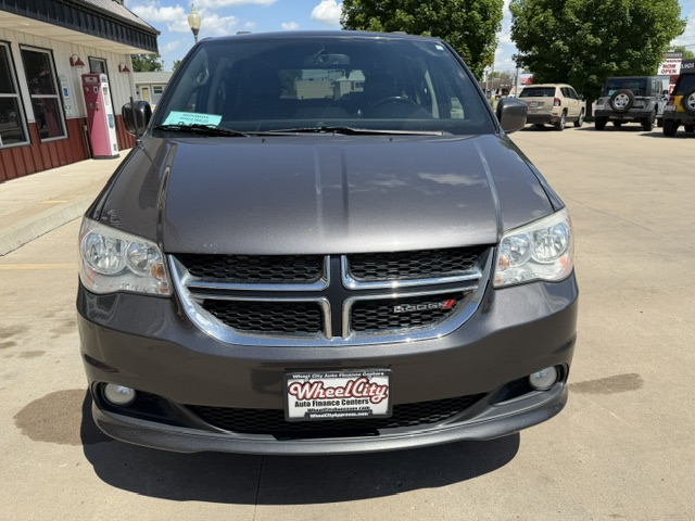 Front view of a gray Dodge minivan in a dealership lot, featuring a chrome grille and headlights, with a green sale sticker on the windshield.