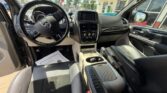 Interior of a pickup-style SUV with a Honda steering wheel, black seats, and a beige center console viewed from the driver’s side; dashboard and touchscreen visible, parked at a dealership with sunlight streaming in.