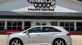 Silver sedan parked in front of a Wheel City Auto Finance Centers building with a red bench nearby, storefronts in background