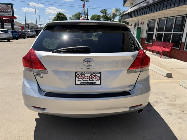 White Toyota SUV seen from the rear in a dealership lot with a Wheel City license plate frame and a red bench outside the building on the right.