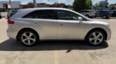 Side view of a silver crossover SUV parked in a sunny parking lot with buildings in the background.