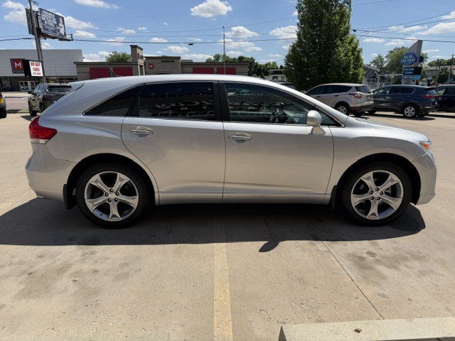 Side view of a silver crossover SUV parked in a sunny parking lot with buildings in the background.