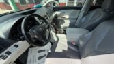 Interior of a gray leather sedan showing the steering wheel, dashboard, and front seats with wood-trim center console inside a showroom setting.