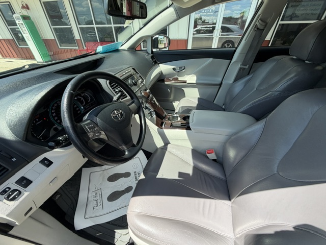 Interior of a gray leather sedan showing the steering wheel, dashboard, and front seats with wood-trim center console inside a showroom setting.