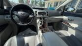 View from the driver’s seat of a beige leather Toyota interior with wood trim center console, steering wheel and front passenger seat visible.