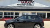 Black Jeep Compass SUV parked in front of Wheel City Auto Finance Centers storefront sign.