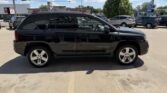 Side view of a black Jeep Compass SUV with chrome wheels parked in a dealership lot.