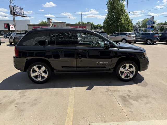 Side view of a black Jeep Compass SUV with chrome wheels parked in a dealership lot.