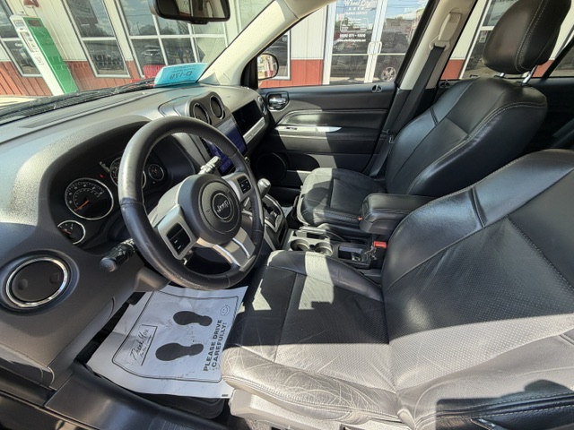 Front interior of a black leather SUV with steering wheel, dashboard, center console, and paper floor mat on the driver's side.