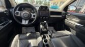 Front seat view of a Jeep interior: steering wheel, center touchscreen, gear shift, and black leather seats.