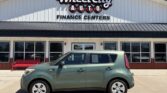 Green compact car parked in front of Wheel City Auto Finance Centers dealership building with large sign above.