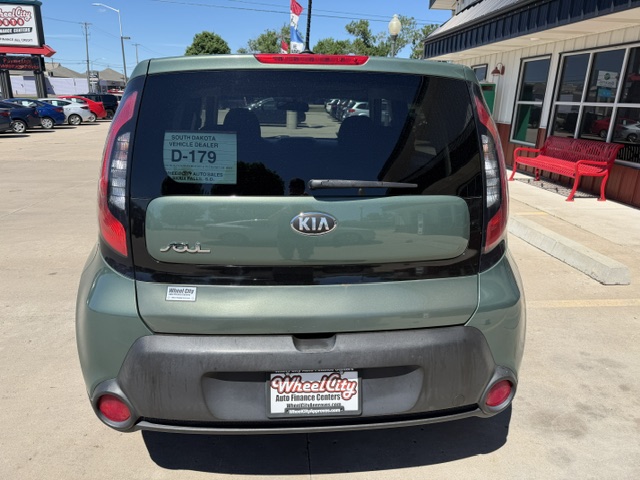 Rear view of a green Kia Soul in a car dealership lot, showing the Kia badge, 'SOUL' lettering, rear windshield wiper, and WheelCity license plate frame.