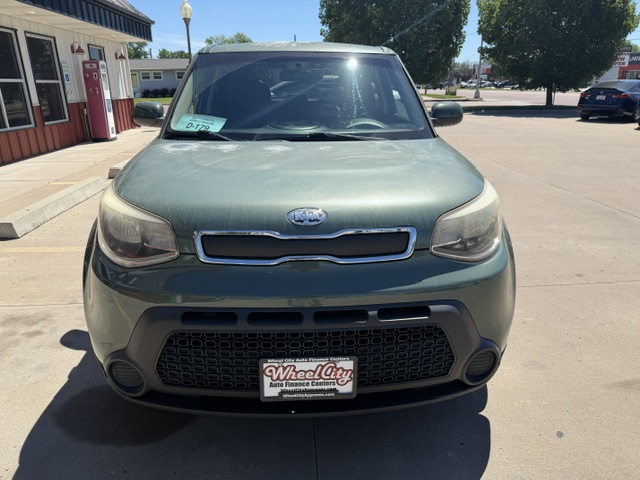 Front view of a green Kia Soul parked at a dealership, with a Wheel City license plate frame on the bumper.