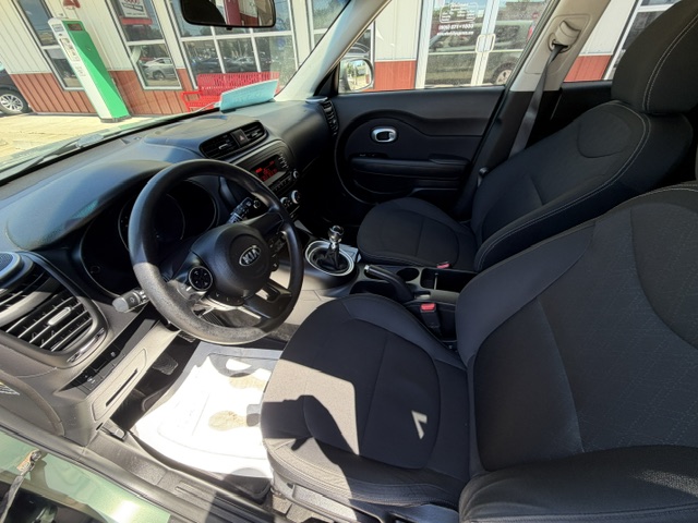 Front interior of a car showing the driver's seat, front passenger seat, steering wheel, manual gear shifter, and center console with dashboard controls.