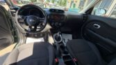 Driver’s-side view of a Kia interior: steering wheel, manual gear shifter, center console with radio and climate controls, and black cloth seats.