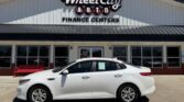 White sedan parked in front of Wheel City Auto Finance Centers storefront on a sunny day.