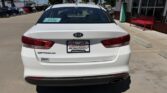 Rear view of a white Kia Optima parked in a dealership lot, with a Wheel City Auto Finance Centers plate frame and a blue sale tag visible on the rear window.