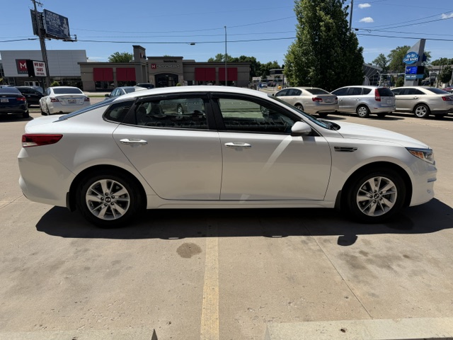 Side view of a white four-door sedan parked in a sunny parking lot with other cars in the background.