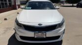 Front view of a white Kia sedan parked in a dealership lot with a Wheel City license plate frame visible on the front bumper.