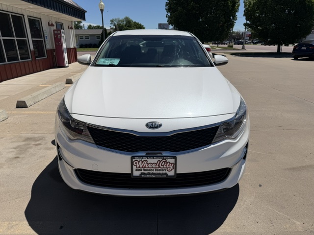 Front view of a white Kia sedan parked in a dealership lot with a Wheel City license plate frame visible on the front bumper.