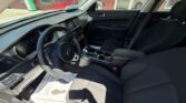 Front interior of a dark cloth sedan: driver’s seat, steering wheel, center console with gear shifter and cupholders, and the front passenger seat; dashboard and windows with sunlight streaming in.