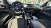 Front interior of a Kia car showing the steering wheel, center console with gear shifter, climate controls, and black cloth seats