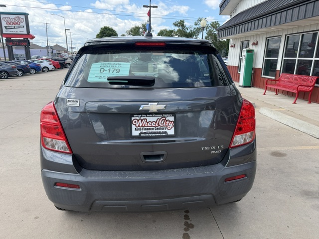 Rear view of a gray Chevrolet Trax LT AWD at a dealership, with a Wheel City license plate frame and window sticker visible on the rear window.