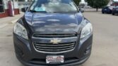 Front view of a dark gray Chevrolet SUV parked in a lot with dealership signs in the background, chrome grille and Chevrolet emblem visible