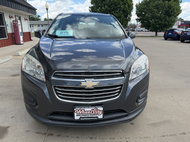 Front view of a dark gray Chevrolet SUV parked in a lot with dealership signs in the background, chrome grille and Chevrolet emblem visible
