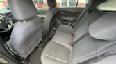 Interior of a car showing the front seats and a three-seat rear bench in gray cloth, with headrests, door panels, and rubber floor mats visible; view through the windows to the outside.