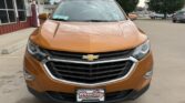 Front view of an orange Chevrolet SUV parked in a lot, showing the grille with bowtie emblem and headlights, dealership plate in front.