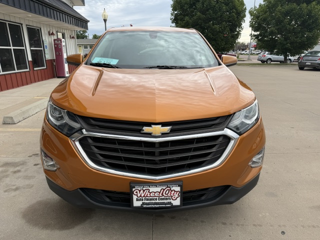 Front view of an orange Chevrolet SUV parked in a lot, showing the grille with bowtie emblem and headlights, dealership plate in front.