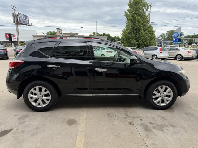 Black mid-size SUV in a parking lot, shown from the side with other cars and a tree in the background.