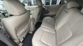 Interior of a beige leather car showing the rear bench seat for three, with visible front seats, headrests, seat belts, and dark floor mats.