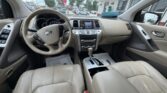 Beige Nissan car interior, front passenger view: steering wheel, center console with screen and gear shifter, beige leather seats.