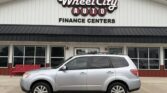 Silver SUV parked in front of Wheel City Auto Finance Centers dealership sign on a white building facade.