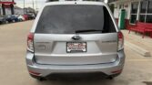 Rear view of a silver Subaru Forester in a dealership lot, with Wheel City Auto Finance Centers plate and red bench nearby.