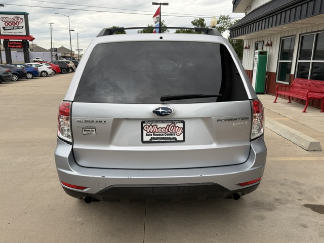 Rear view of a silver Subaru Forester in a dealership lot, with Wheel City Auto Finance Centers plate and red bench nearby.
