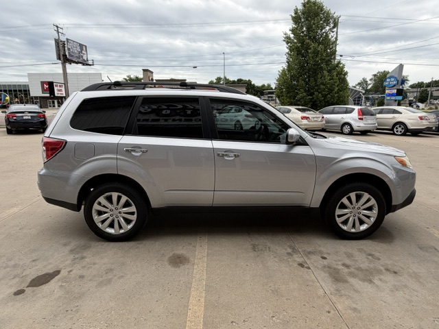 Side view of a silver SUV with roof rails parked in a dealership lot, with other cars and trees in the background.