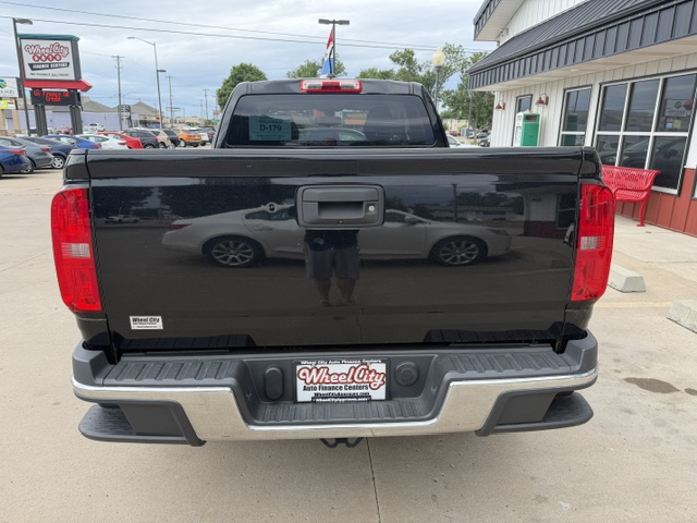 Rear view of a black pickup truck in a car dealership lot; chrome bumper, red taillights, and a Wheel City license plate frame visible on the tailgate.