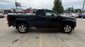 Black four-door pickup truck parked in a dealership lot, seen from the side with chrome wheels and running boards.